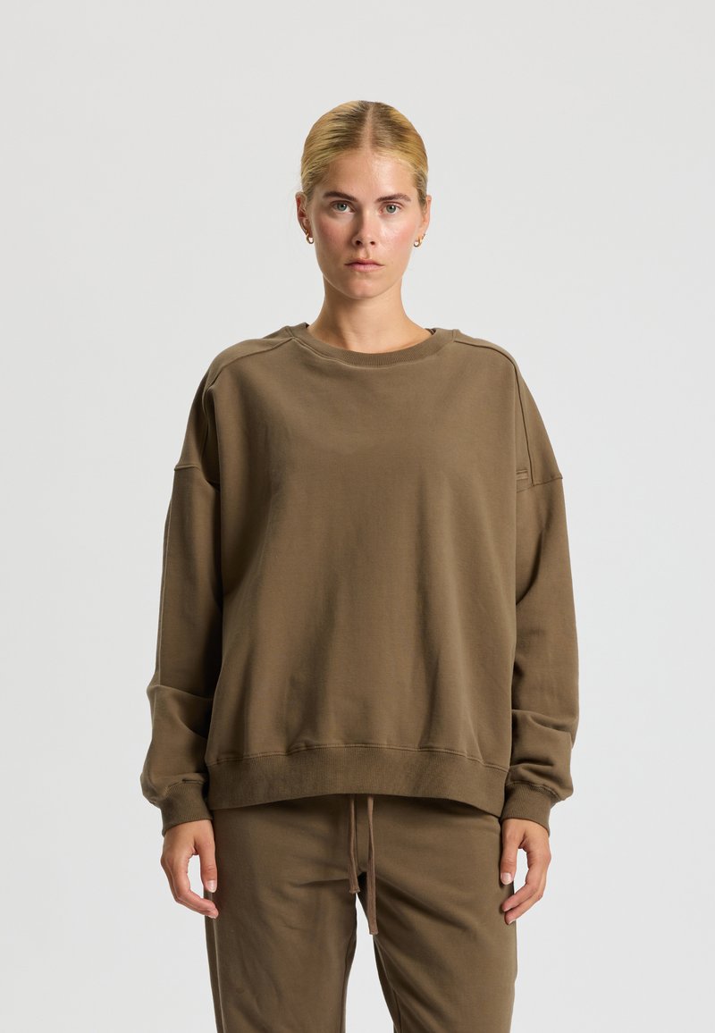 Brown oversized sweatshirt in soft cotton blend, featuring a crew neck, dropped shoulders, and ribbed cuffs. Paired with matching pants.