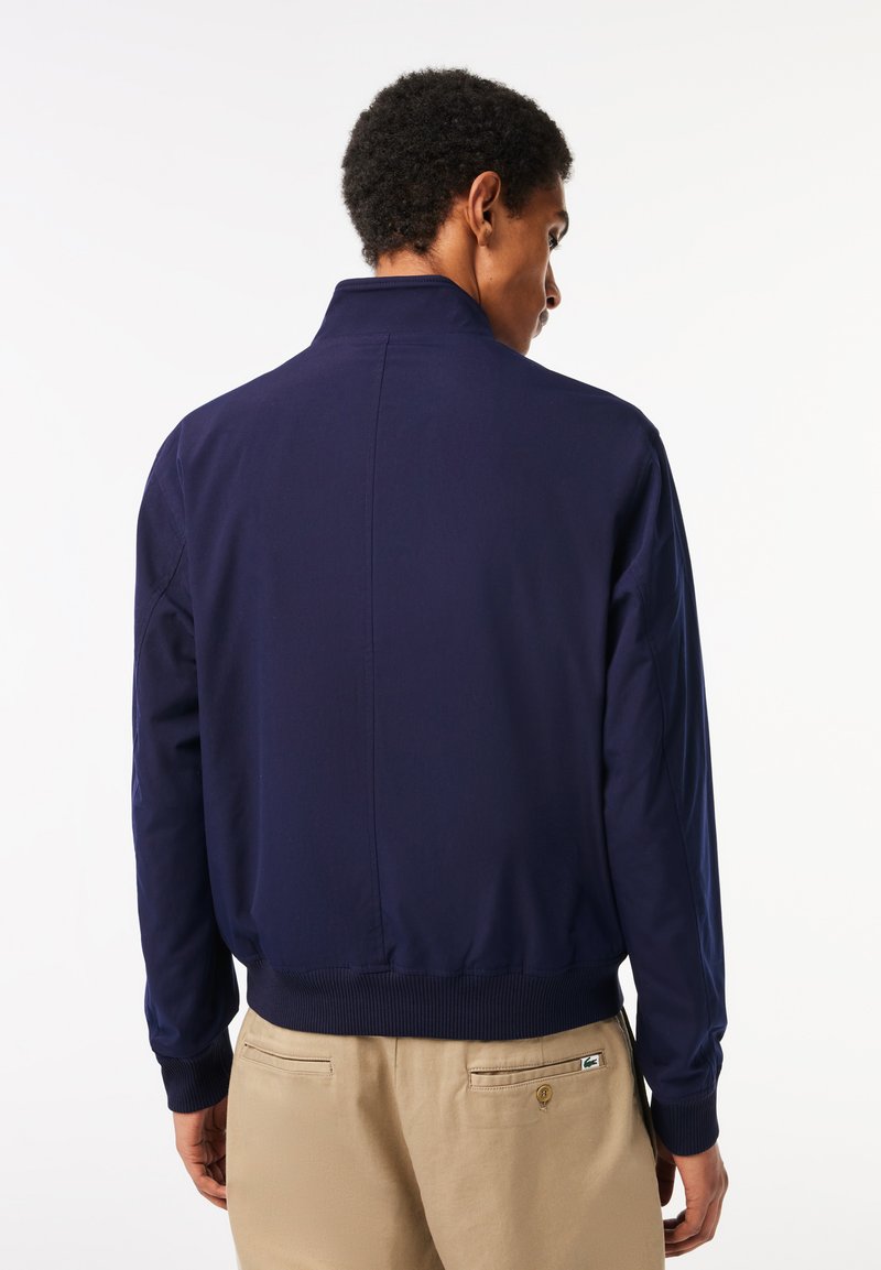 Veste de pilote navy avec col et poignets côtelés, fabriquée dans un tissu lisse et léger, avec un ourlet droit. Design minimaliste sans ornements.