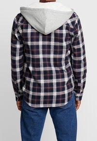 Checkered flannel shirt in navy, white, and red, with a gray, fleece-lined hood and long sleeves; button cuffs and back yoke design.
