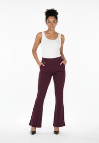 Bordowe dzwony o gładkiej fakturze z kieszeniami, zestawione z dopasowanym białym topem na ramiączkach. Całość uzupełniają czarne szpilki.