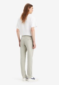 Pantaloni dritti grigio chiaro realizzati in morbido twill di cotone, con due tasche posteriori e un piccolo etichetta del marchio sulla cintura, abbinati a una t-shirt bianca.