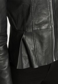 Černá kožená bunda s přiléhavým střihem, peplum detaily a předním zipem. Hladký povrch a dlouhé rukávy s švy.
