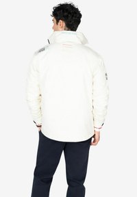 Chaqueta blanca con cuello alto, tejido texturizado, logotipos bordados en los hombros y colores de acento contrastantes en los puños.
