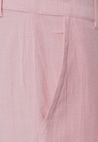 Růžová lněná tkanina s texturovaným povrchem, která má přední kapsu a pečlivě šité švy, což vytváří jemný a lehký vzhled.