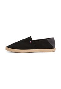 Zapato de lona negro tipo slip-on con punta afilada, suela de cuerda color tostado y acentos grises en la parte trasera. Cuenta con un pequeño logo multicolor en el lado.