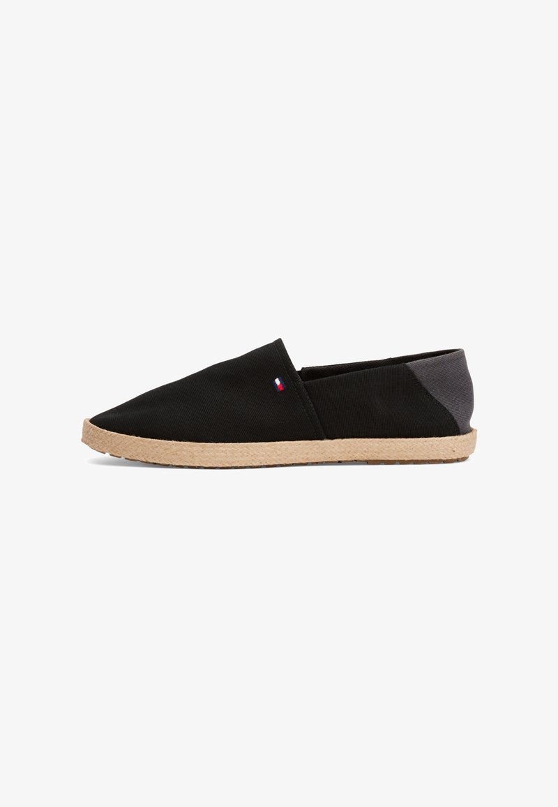 Sandal de tela negra, tipo slip-on, com bico apontado, sola de corda castanha e detalhes cinzentos na parte de trás. Apresenta um pequeno logótipo multicolorido de lado.