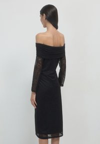 Schau-schulterfreies schwarzes Kleid mit langen Spitzenärmeln, taillierter Textur, knielanger Länge und dezentem Blumenmuster auf dem Stoff.