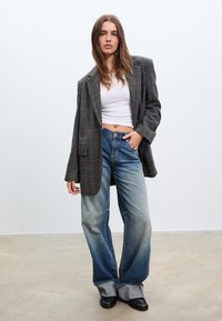 Oversized grijze geruite blazer met brede revers, gecombineerd met lichtblauwe high-waisted jeans. Getextureerde stof en ontspannen pasvorm, gedragen met zwarte schoenen.