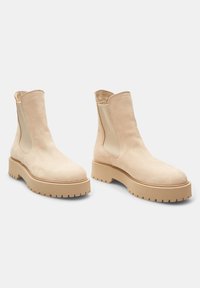 Botine de gleznă bej din suede cu panouri elastice laterale, vârf rotund și talpă din cauciuc chunky cu textură pentru aderență.