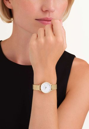 Montre-bracelet en or avec un cadran blanc rond, au design minimaliste, et un bracelet en maillons métalliques avec des accents dorés polis.