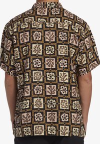 Camisa de manga corta en negro con un diseño colorido y estampado que presenta motivos florales y formas geométricas en beige, marrón y rosa.