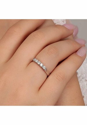 Silberner Ring mit fünf klaren runden Steinen, die in einem eleganten Band eingefasst sind, präsentiert auf einer Hand mit sanft manikürten Nägeln.