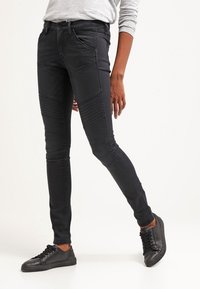 Jeans ajustados negros con paneles texturizados y detalles de costura, hechos de tela de mezclilla, combinados con zapatillas negras.