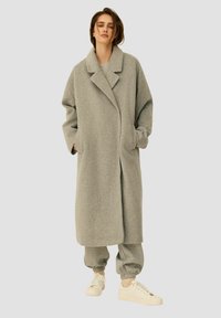 Szary wełniany płaszcz z wyciętym kołnierzem, długimi rękawami i bocznymi kieszeniami, w zestawie z dopasowanymi szarymi dresami i białymi trampkami.