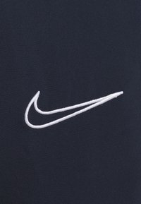 Vit broderad Nike swoosh-logotyp på en mörk marinblå tygbakgrund, som visar varumärkets emblem på textilytan.