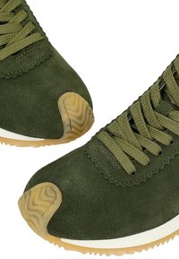 Sneakers in suede verde con punte tonde, lacci texturizzati e suola in gomma di un leggero color tan. Presentano un sottopiede bianco e un motivo a zigzag sulla suola.