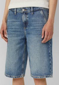 Shorts en jean en tissu bleu clair, avec une coupe décontractée, des poches avant et un ourlet retroussé avec des détails de couture visibles.