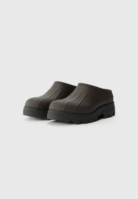 Sötétbarna, slip-on klumpák, struktúrált felülettel, bordázott mintázattal és vastag fekete talppal, amely tapadást biztosító mintázattal rendelkezik.
