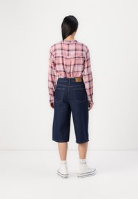 Karirana roza majica s dolgimi rokavi v kombinaciji z temno modrimi jeans kraticami do kolen, ki imajo dve zadnji žep in zavito obrobo.