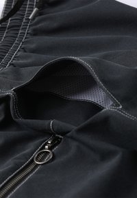 Shorts atletici negri cu un buzunar cu fermoar, având un exterior moale și neted și căptușeală din plasă. Detalii contrastante de cusătură albă vizibile.