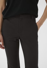Black tailored trousers with a smooth fabric, slim fit, and side pockets. Features a flat front and subtle crease detail.