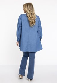 Hellblaue Denim-Tunika mit abgerundetem Saum und langen Ärmeln, kombiniert mit passenden, taillierten Jeans und silbernenHigh Heels.