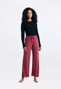 Zwart langemouwen top en wijde bordeauxrode broek met een trekkoord in de taille. Gladde, zachte stof met een losse pasvorm.