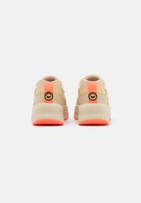 Beige sneakers with a textured upper, bright coral accents on the sole and heel, featuring a circular logo and reinforced back tab.