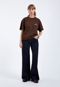 Brown cotton t-shirt with short sleeves, featuring white embroidery. Paired with wide-leg dark denim jeans. Simple design, solid colors.