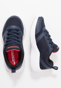 Baskets Skechers bleu marine en mesh, avec un col rembourré, une semelle blanche et une touche de rouge sur la doublure intérieure et le logo. Design léger.