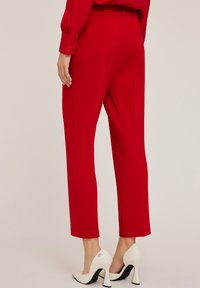 Pantalons ajustés rouges avec une coupe droite, en tissu lisse, et deux poches arrière, associés à des chaussures à talons hauts blanches.