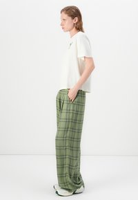Loose-fitting cream T-shirt with a graphic, paired with green plaid trousers. The trousers have a relaxed cut and pockets. White sneakers complete the look.
