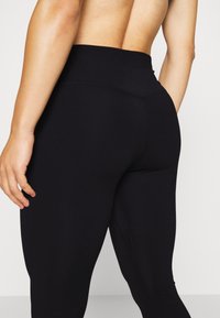Leggings neri a vita alta con una texture liscia, caratterizzati da un design aderente e una cucitura sottile lungo il lato.