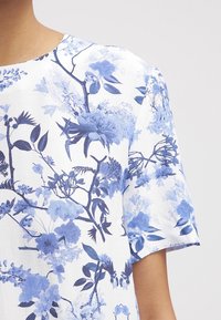 Blusa con estampado floral en tonos azules sobre un fondo blanco, de mangas cortas y con una textura de tela suave y ligera.