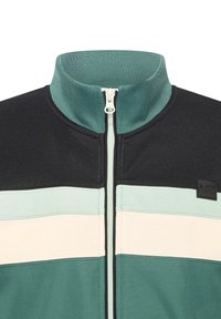 Giacca con zip e colletto alto caratterizzata da un design a blocchi di colore in verde scuro, teal, crema e nero, tessuto testurizzato con logo in evidenza.