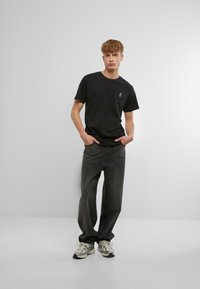 Svart bomulls T-skjorte med en liten logo på brystet, kombinert med løstsittende mørke jeans og flerfargede joggesko.