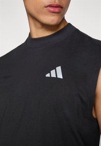 Μαύρο αμάνικο αθλητικό τοπ με ψηλό λαιμό, κατασκευασμένο από λείο ύφασμα. Διαθέτει ασημί λογότυπο και υφασμένη ραφή στον ώμο.