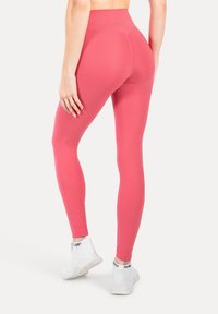 Leggings ajustados de cintura alta en un tejido de color rosa brillante con una textura suave. Combinándolos con zapatillas deportivas blancas con detalles en negro.