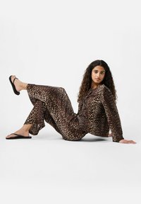 Set di loungewear con stampa leopardata in tonalità di marrone e beige, maniche lunghe, pantaloni larghi, abbinato a ciabatte nere. Tessuto morbido, vestibilità rilassata.