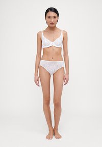 Weißes Spitzen-Bralette mit gewellten Kanten, kombiniert mit passenden Spitzen-Hipster-Unterhosen. Beide zeigen florale Muster und eine sanfte Textur.