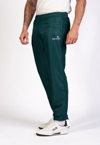 Donkergroene sportbroek met elastische taille, taps toelopende benen en logodetail. Gemaakt van gladde, lichte stof. Gepaard met witte sneakers.