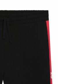 Sorte sweats med ribbet talje, prydet med en solid rød sidebjælke og hvid tekstdetalje på højre ben. Blødt stof.