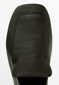 Černá kožená mokasína s texturovaným povrchem, zaoblenou špičkou a minimalistickými švy na vrchní části. Viditelná hladká vnitřní podšívka.