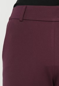 Burgunderrote Hose mit glatter Textur, ausgestattet mit einem flachen Bund vorne und einem maßgeschneiderten Schnitt. Keine sichtbaren Verschlüsse oder Muster.