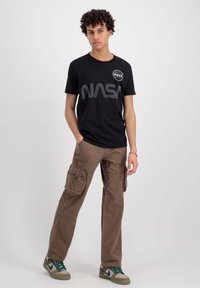 Zwarte katoenen T-shirt met een NASA-logo op de borst, gecombineerd met lichtbruine cargo-broeken met grote zijzakken en een relaxed fit.