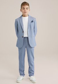 Ljusblå blazer med bruna knappar, vit t-shirt, matchande ljusblå byxor och vita sneakers. Strukturerad tyg med skräddarsydd passform.