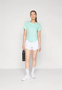 Világoszöld rövid ujjú ing, fehér sportshort, fekete vízpalack, fehér sportcipő és zokni. Egyszerű dizájn és laza szabás.