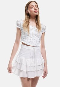 Witte crop top met pofmouwen en een bloemenpatroon; gecombineerd met een gelaagde witte rok met een trekkoord in de taille.