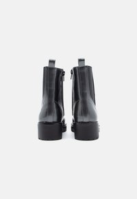 Černé kožené kotníkové boty s lesklým povrchem, bočním zipem, nízkým podpatkem a poutky vzadu pro snadné obouvání.