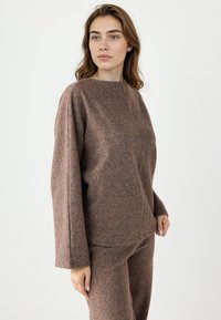 Maglione marrone di lana con collo alto e maniche lunghe, caratterizzato da una vestibilità leggermente ampia e una texture liscia. Design semplice senza motivi.